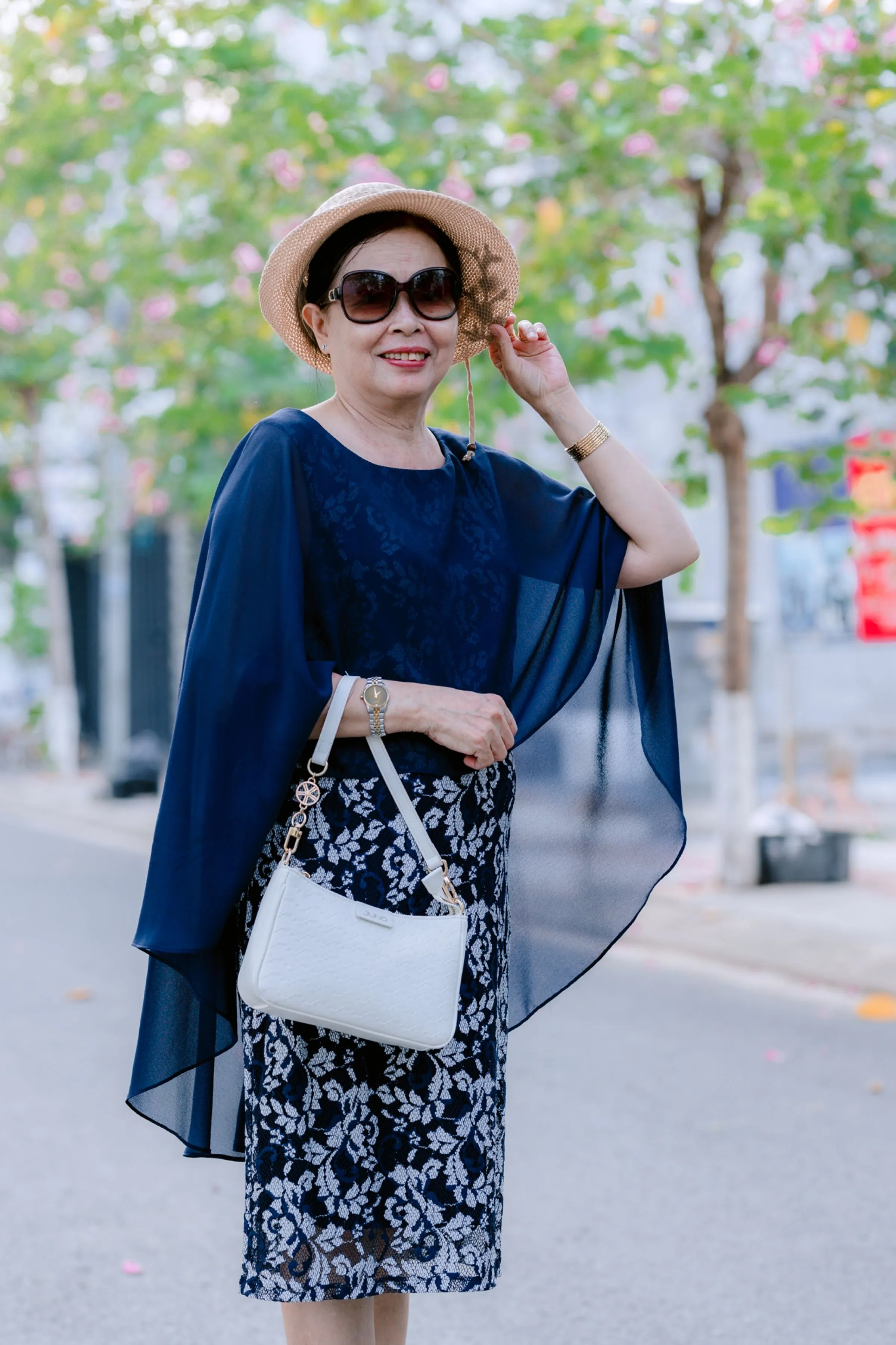 Stylish older woman in a navy wrap, sunglasses and straw hat on a city street