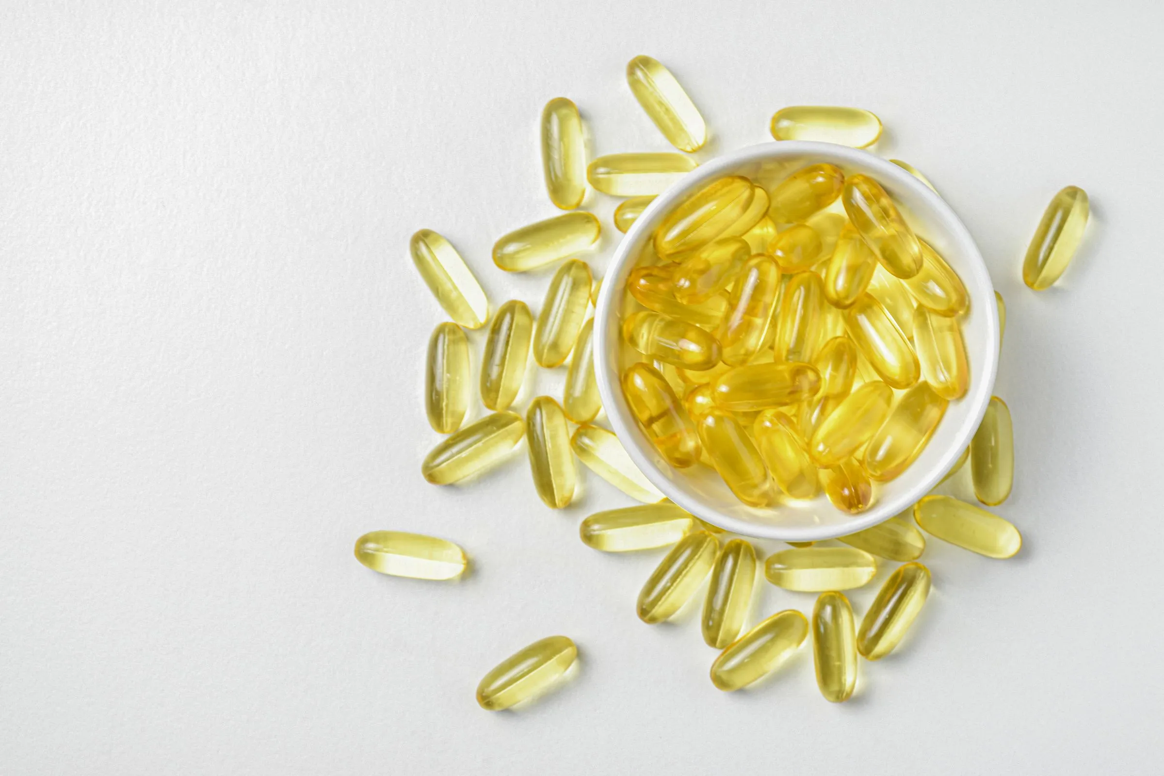 Golden softgel capsules in a white ceramic bowl